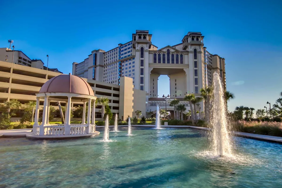 An elegant exterior shot featuring a tranquil fountain, a charming gazebo, and the resort's building architecture. The area is landscaped and inviting, ideal for relaxing after a day by the beach or pool.