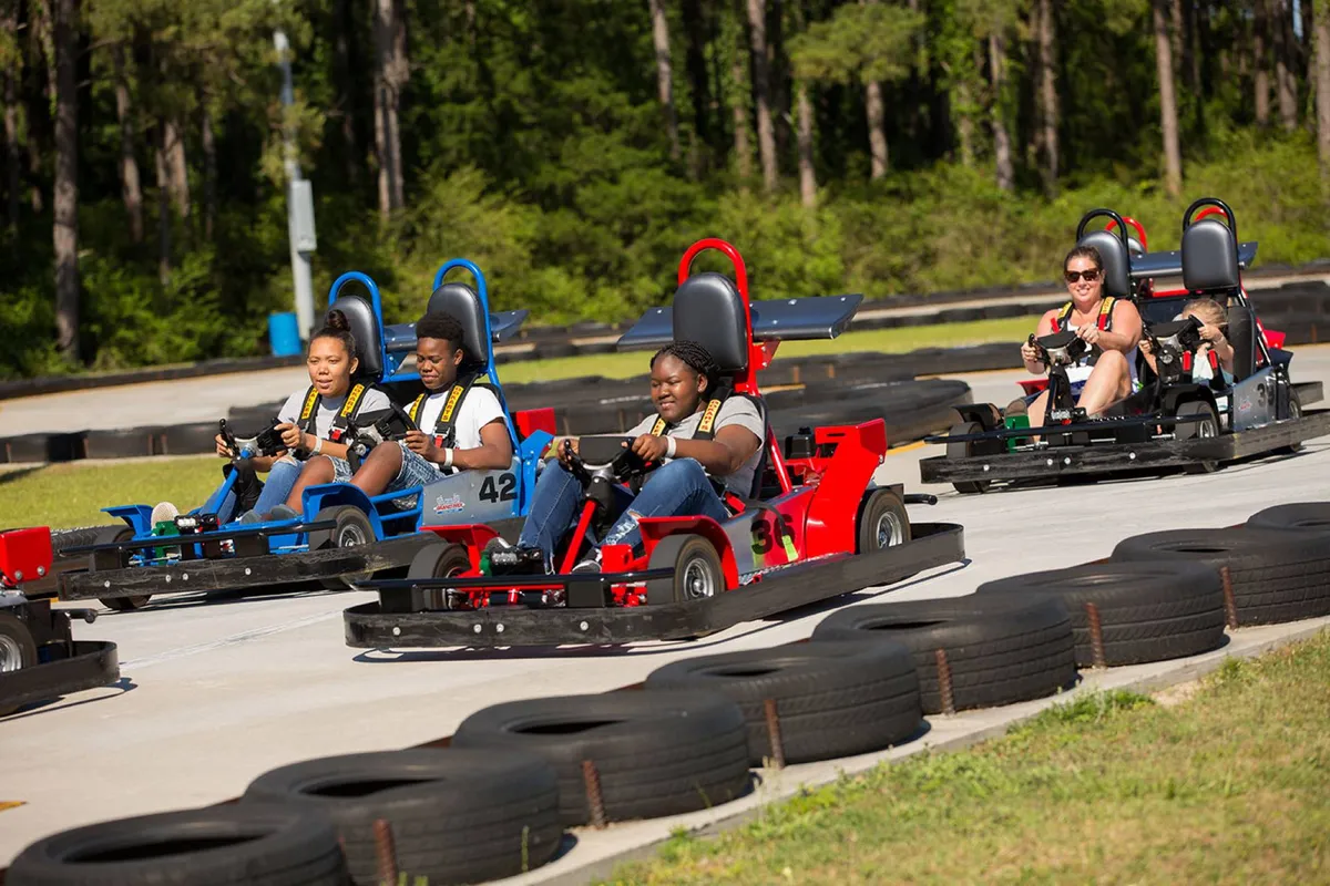 A dynamic exterior scene at a go-kart racetrack, capturing participants in action and families enjoying a thrilling racing experience. The image conveys motion, excitement, and group bonding.