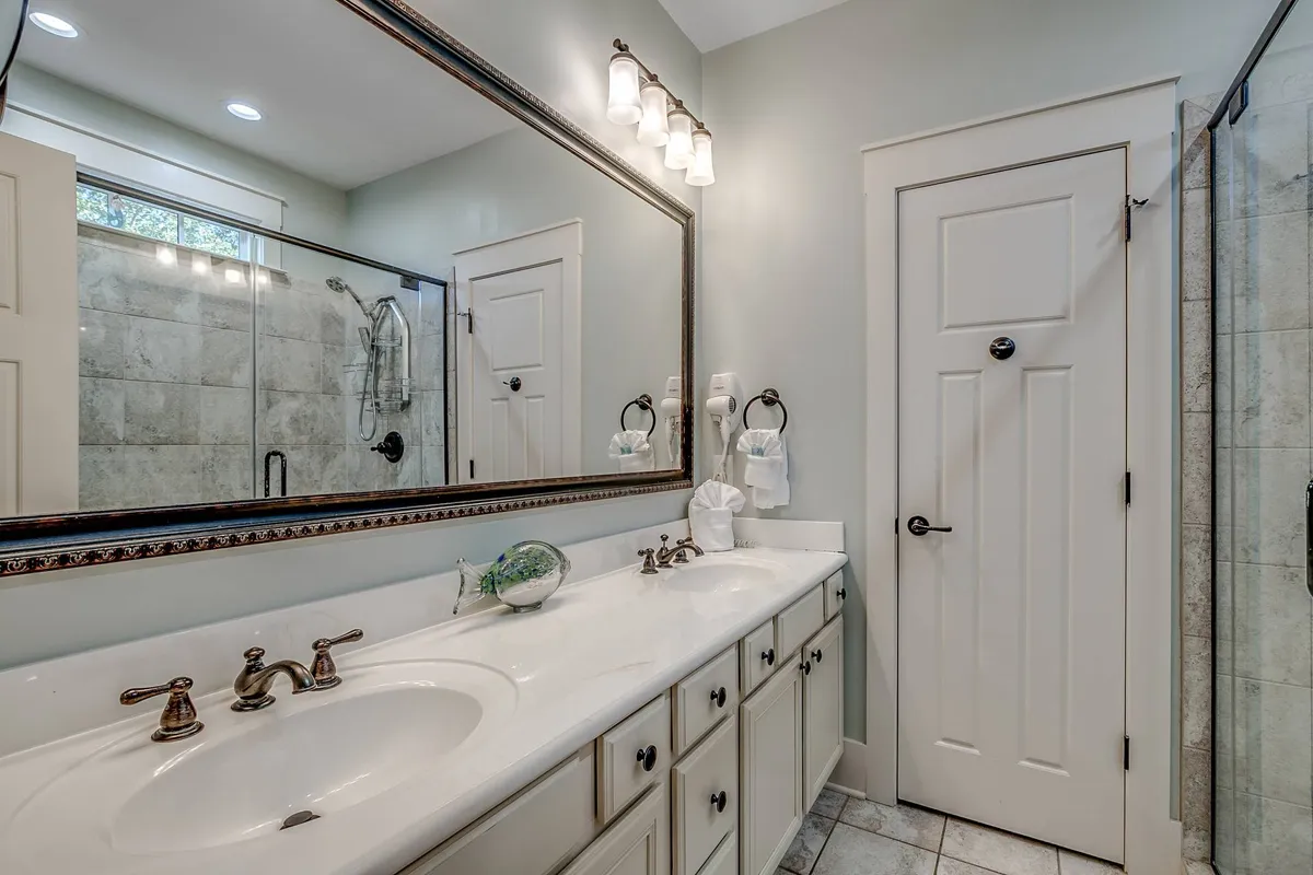 A serene ensuite bathroom with a large double sink vanity, expansive mirror, and a glass-enclosed shower. The space is bright and refreshing, offering a touch of hotel-like luxury.