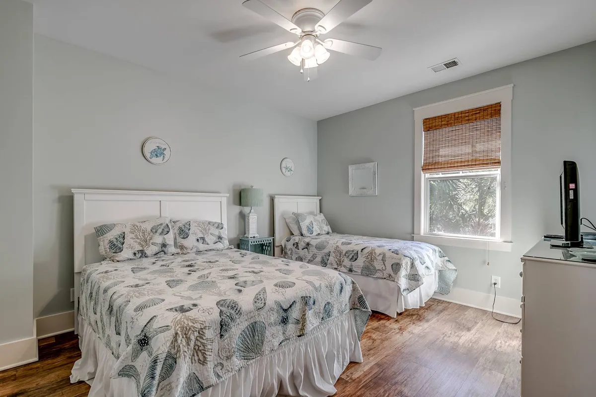 A guest bedroom with two beds adorned in decorative bedspreads, a ceiling fan for comfort, and a window letting in natural light. The beds are arranged to provide both privacy and togetherness, ideal for siblings or friends.