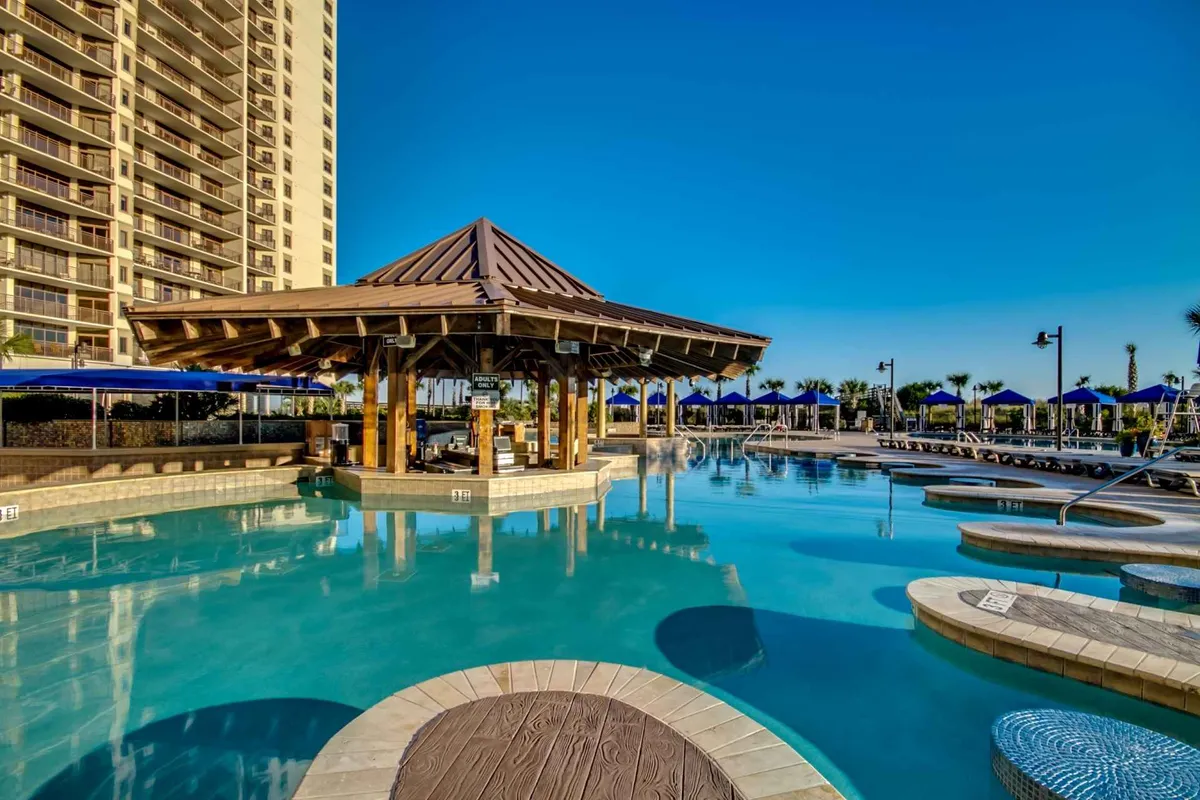 A close-up of a sparkling swimming pool bordered by comfortable lounge chairs and a shaded poolside cabana. The setting is serene yet social, ideal for sunbathing, relaxing, or gathering with friends.