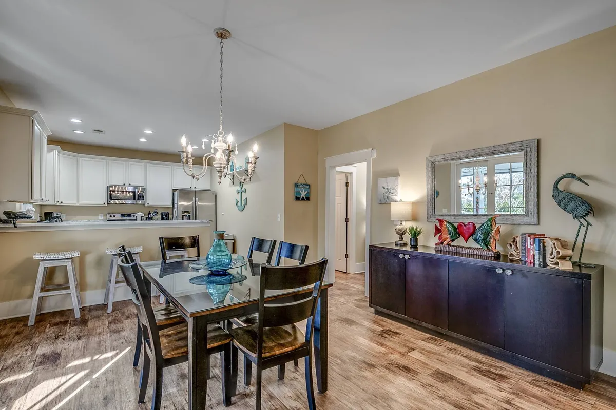 A cozy dining area with a large table set beneath a charming chandelier, decorative sideboard items, and a view into the kitchen. The space is ready for family meals, celebrations, or planning the next day's adventures.
