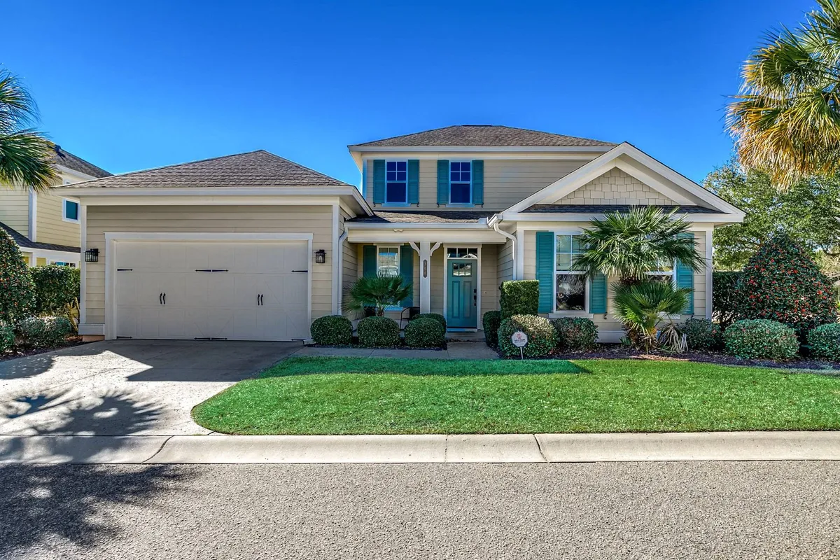 The image showcases the charming exterior of a single-family house in North Myrtle Beach, featuring a welcoming front porch, classic shutters framing large windows, a well-kept landscaped garden, and a spacious garage. The serene, inviting setting hints at relaxing mornings on the porch and memorable gatherings with family or friends.