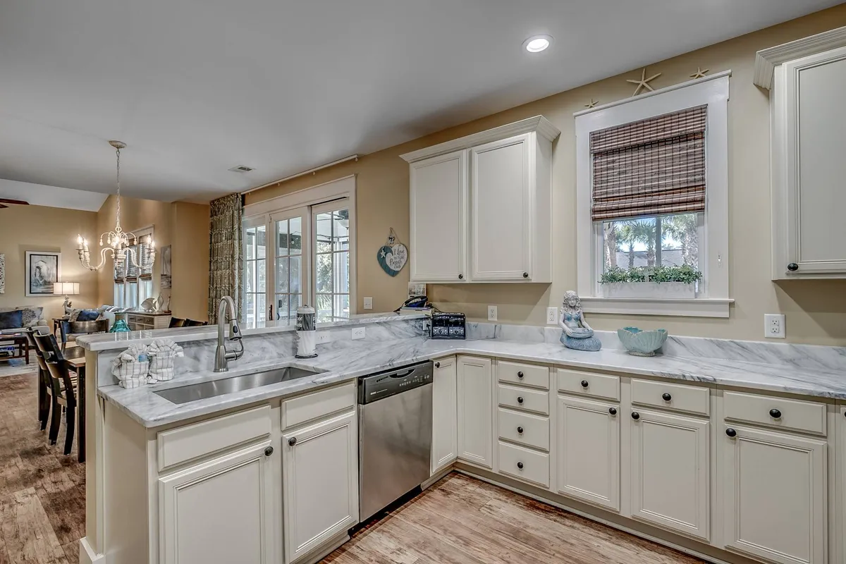 A bright kitchen highlighted by a sunlit island with a marble countertop, seamlessly connecting to a dining area. The layout is both functional and stylish, providing a place for cooking, entertaining, or a quick breakfast before heading out to enjoy local perks.